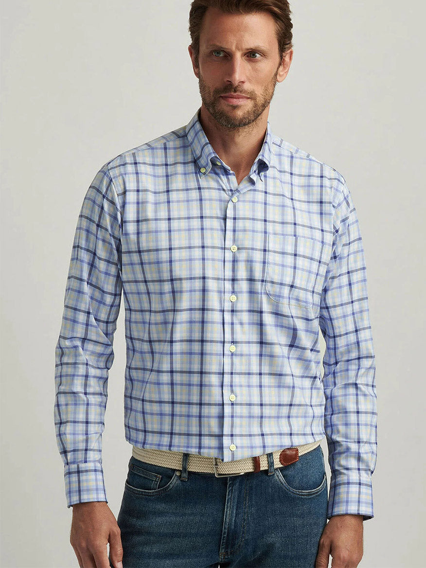 A man wears a Peter Millar Chambly Crown Lite Cotton-Stretch Sport Shirt in Morning Blue with jeans, standing against a plain background.