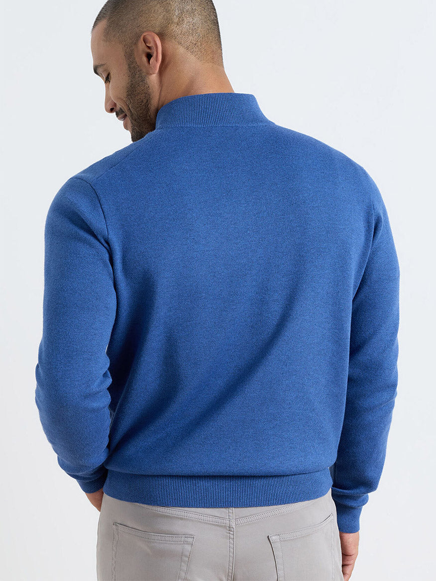 Man with his back turned, wearing a Peter Millar Coolspun Lite Cotton Quarter-Zip Sweater in Windsor Blue and light gray pants against a plain light background.