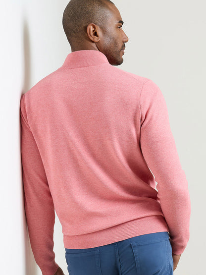 A man wearing a Peter Millar Coolspun Lite Cotton Quarter-Zip Sweater in Venetian Pink and classic-fit blue pants stands facing a white wall, shown from the back.
