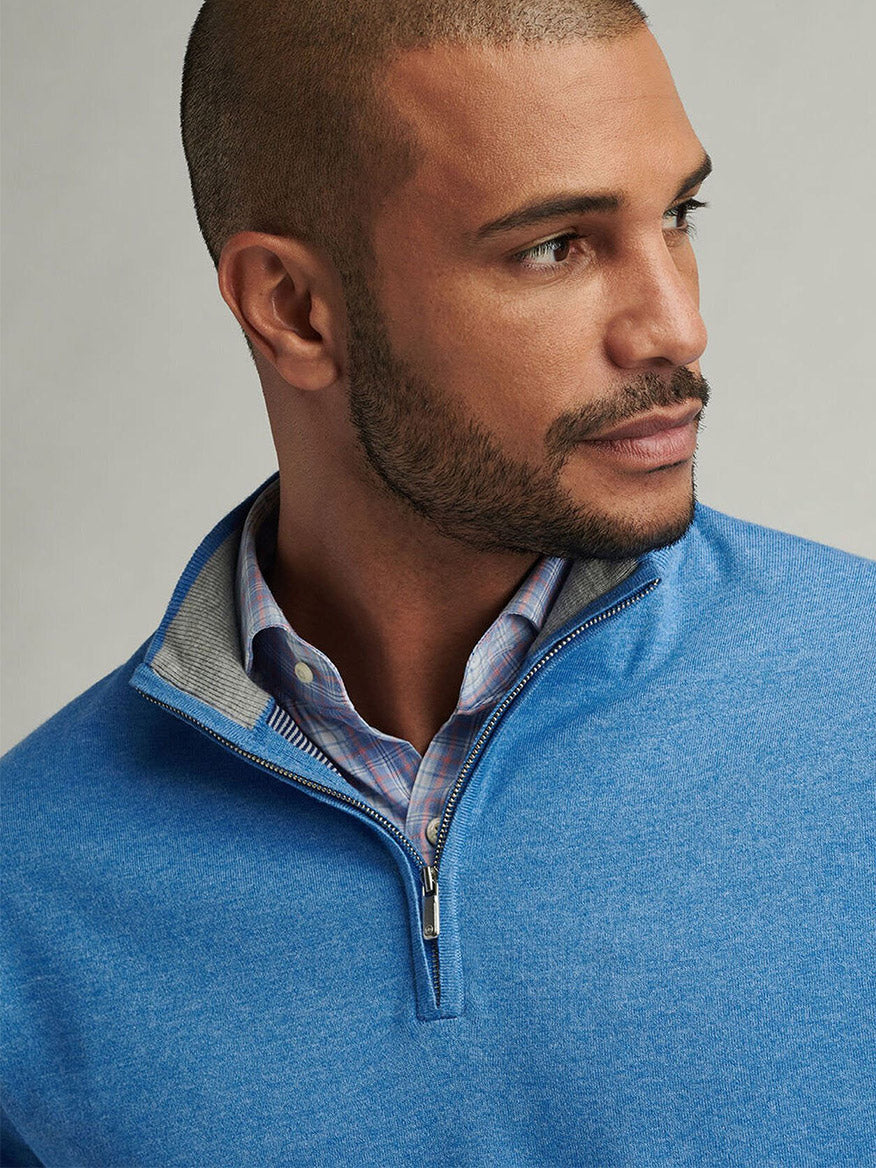 A person with a close-cropped haircut and beard wears a Peter Millar Coolspun Cotton Quarter-Zip Sweater in Blue Poppy over a plaid shirt, looking to the side against a neutral background.