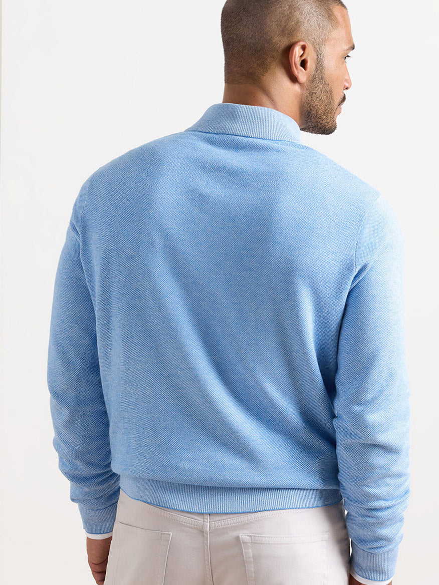 Man stands with his back to the camera, wearing a Peter Millar Coolspun Lite Birdseye Quarter Zip Sweater in Bluebird and beige pants against a plain background.