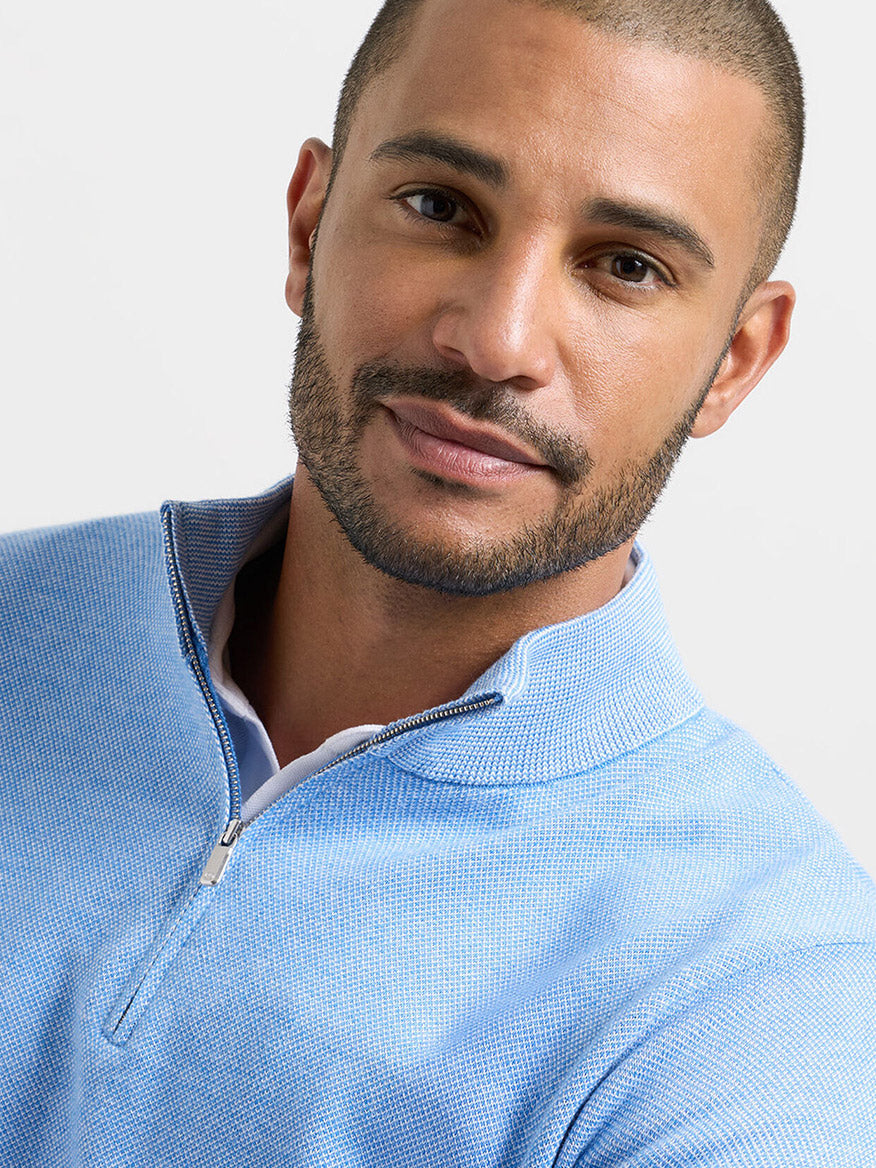 Man with short hair and trimmed beard wears a Peter Millar Coolspun Lite Birdseye Quarter Zip Sweater in Bluebird, known for moisture-wicking fabric, while looking at the camera against a plain background.