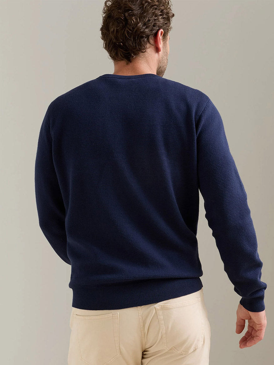 A man is shown from the back wearing a Peter Millar Coolspun Lite Textured Crewneck Sweater in Navy and beige pants against a plain background.
