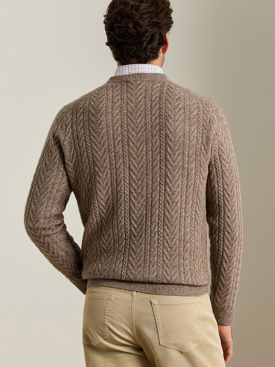 Back view of a person wearing a tan Peter Millar Crescent Cable Crewneck Sweater in Sawgrass over a plaid button-down shirt and tan pants.