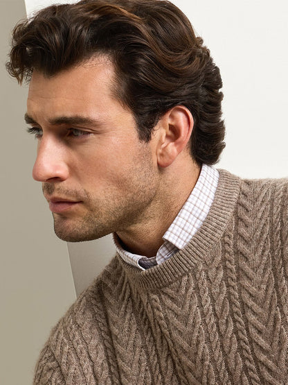 A man wearing a Peter Millar Crescent Cable Crewneck Sweater in Sawgrass over a light-colored checkered button-down shirt.