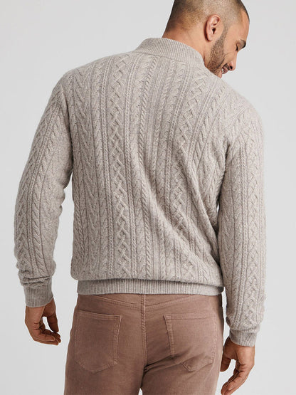 A man faces away in a Peter Millar Crescent Ridge Cable Quarter-Zip Sweater in Light Elm and light brown pants, standing against a plain background.