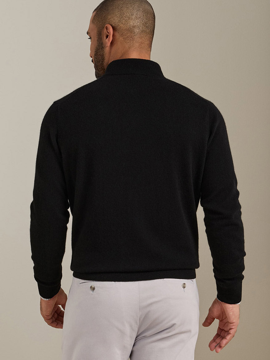 Back view of a man wearing a black Peter Millar 25th Anniversary Cashmere Quarter-Zip Sweater and light-colored trousers.