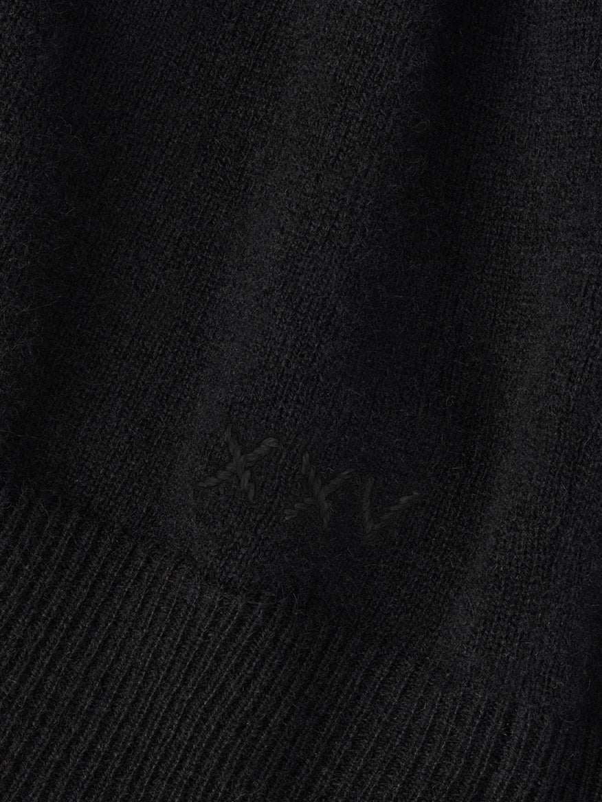 Close-up of a black Peter Millar 25th Anniversary Cashmere Quarter-Zip Sweater with the Roman numeral “XXV” embroidered in matching black thread.