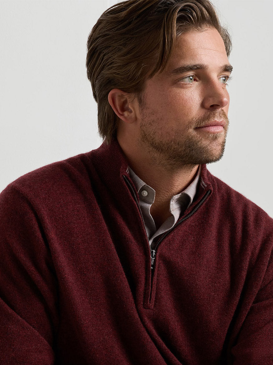 A man wears a classic fit Peter Millar 25th Anniversary Cashmere Quarter-Zip Sweater in Bordeaux over a light-colored button-down shirt.