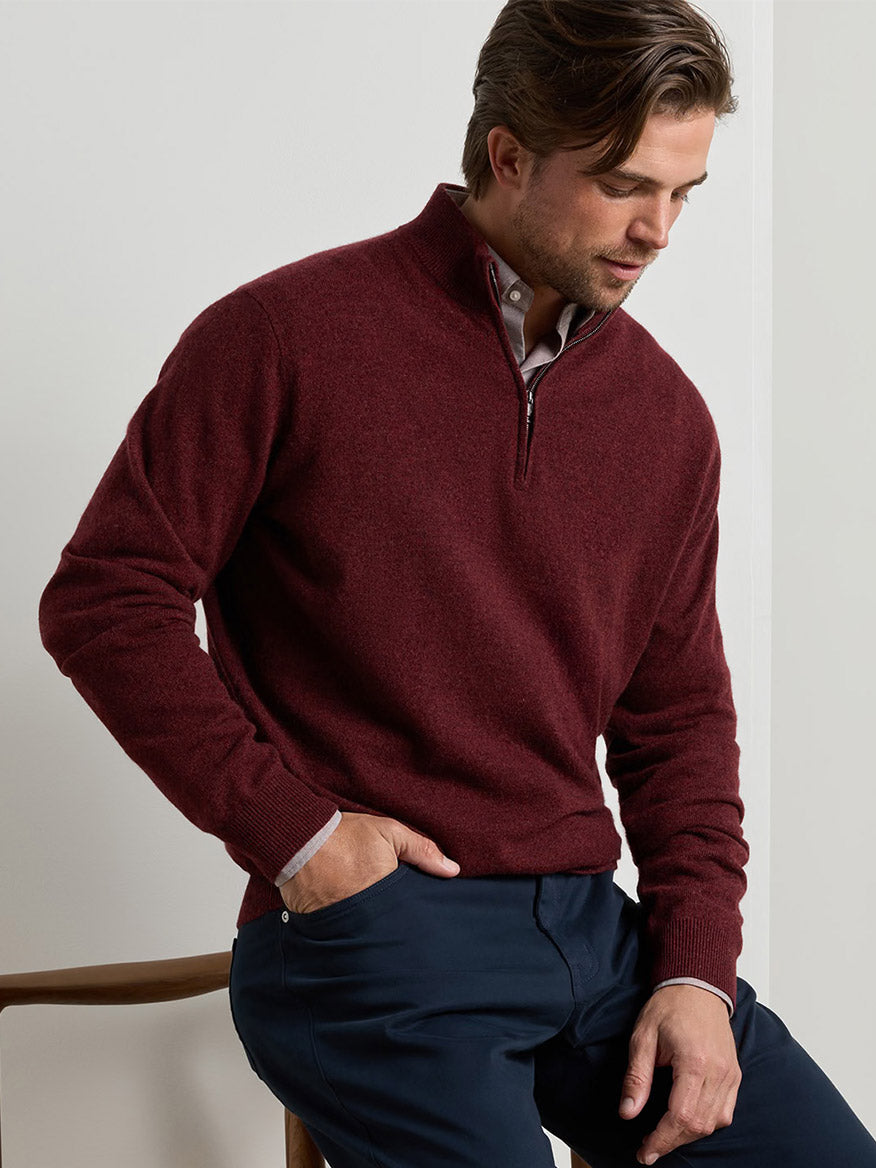 Man wearing a dark red Peter Millar 25th Anniversary Cashmere Quarter-Zip Sweater over a light-colored button-down shirt and dark trousers.