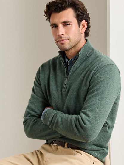 Man wearing a Peter Millar 25th Anniversary Cashmere Quarter-Zip Sweater in Ivy with a small “XXV” embroidered on the lower left hem, layered over a collared shirt and tan trousers.