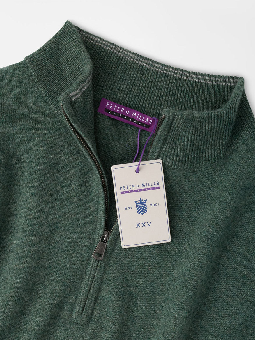 Dark green Peter Millar 25th Anniversary Cashmere Quarter-Zip Sweater in Ivy with a limited-edition anniversary hangtag attached to the zipper pull.