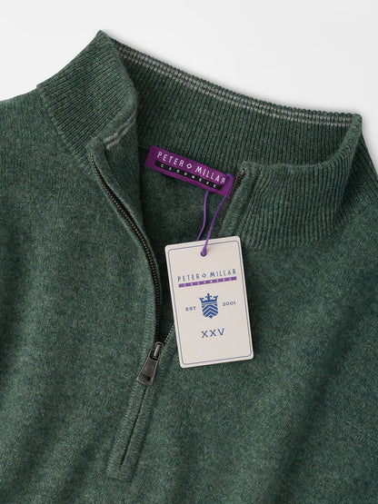 Dark green Peter Millar 25th Anniversary Cashmere Quarter-Zip Sweater in Ivy with a limited-edition anniversary hangtag attached to the zipper pull.