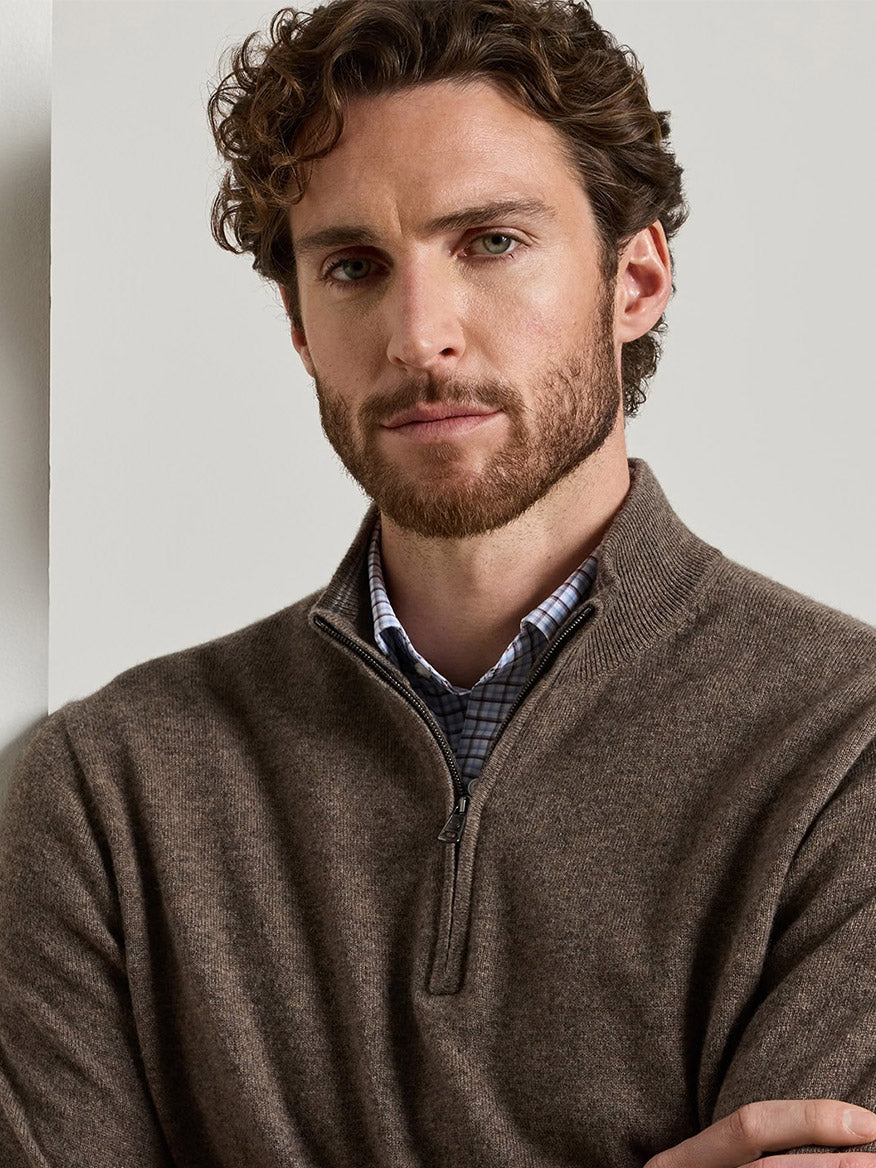 A man wearing a Peter Millar 25th Anniversary Cashmere Quarter-Zip Sweater in Sawgrass over a blue and white patterned shirt.