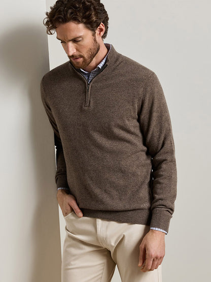 A man wears a brown Peter Millar 25th Anniversary Cashmere Quarter-Zip Sweater in Sawgrass over a plaid button-down shirt and beige trousers.