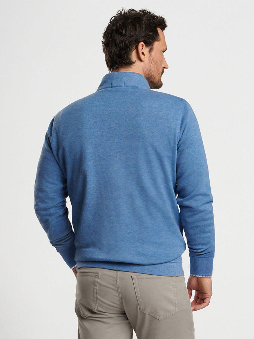 A man with short curly hair and a beard is seen from behind wearing a Peter Millar Crown Comfort Pullover in Astral Blue and gray pants.