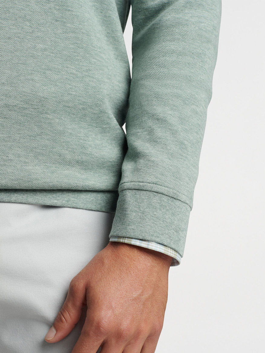 A close-up of a person's side torso showing a Peter Millar Crown Comfort Pullover in Tea Leaf with a folded cuff and a hand resting on a pale waistband.