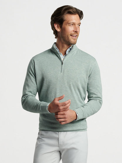 Man in a Peter Millar Crown Comfort Pullover in Tea Leaf and white pants posing with hands gently clasped.