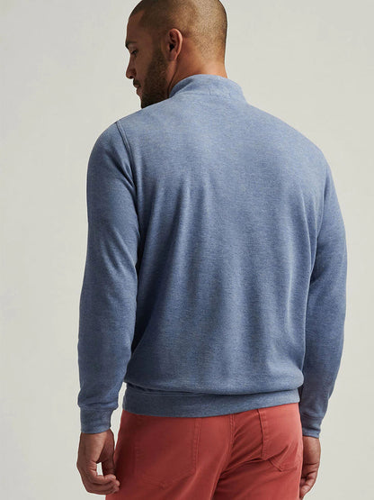 A person in a Peter Millar Crown Comfort Pullover in Blue Freesia and red pants is standing and looking to the side.