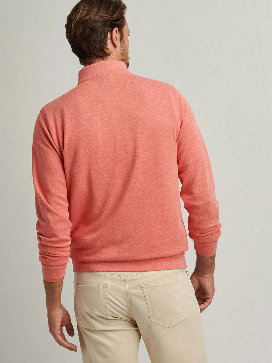 A person with their back to the camera wears a Peter Millar Crown Comfort Pullover in Geranium and beige pants, standing against a plain gray background.