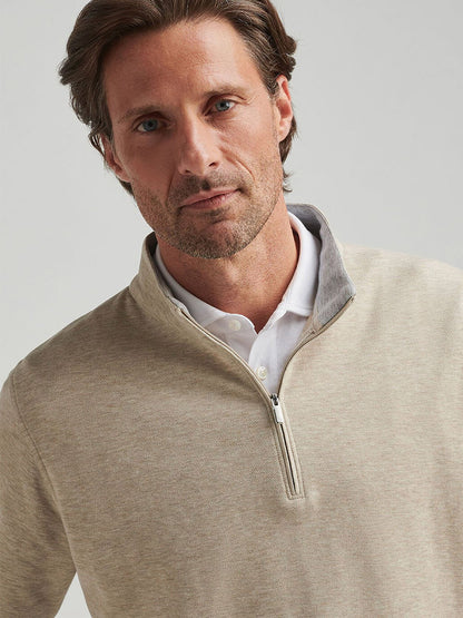 A brown-haired, bearded man stands against a neutral background wearing the Peter Millar Crown Comfort Pullover in Stone as a lightweight layer over his white shirt.