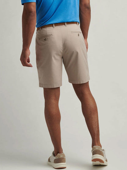 A man faces away, wearing a blue polo shirt, beige sneakers, and Peter Millar Crown Comfort Short in Khaki against a plain background.