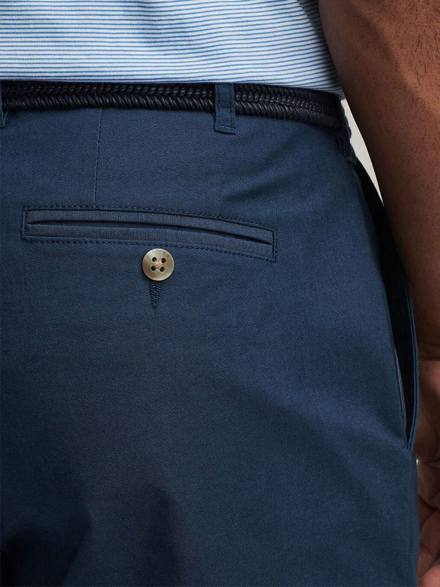 Close-up of Peter Millar Crown Comfort Short in Washed Navy featuring a plain weave back pocket with button closure, styled with a braided black belt and a striped shirt—ideal for those who appreciate versatile classics.