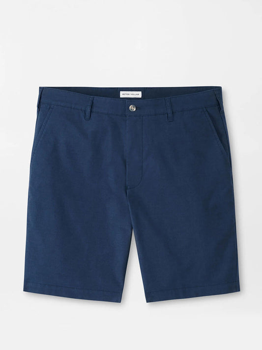 The Peter Millar Crown Comfort Short in Washed Navy, made from four-way stretch plain weave fabric, features side pockets, a button closure, and belt loops, shown laid flat on a light background.