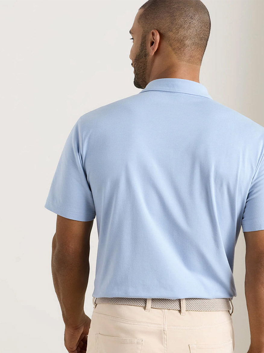 A man is shown from the back wearing a Peter Millar Crown Flex Cotton Polo in Cloudy Blue, classic fit, tucked into beige pants.
