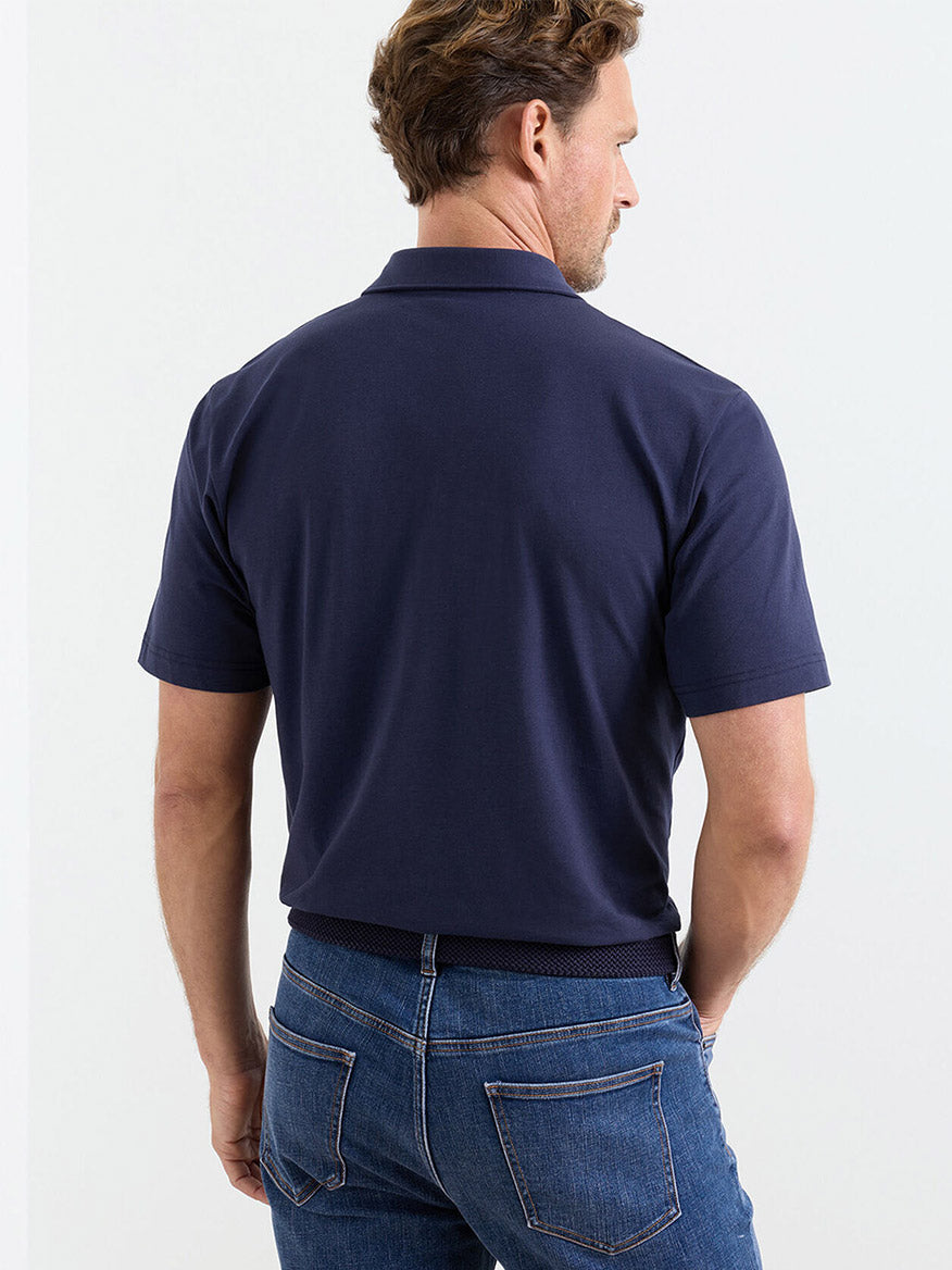 A man stands facing away from the camera, wearing a navy Peter Millar Crown Flex Cotton Polo and blue jeans.