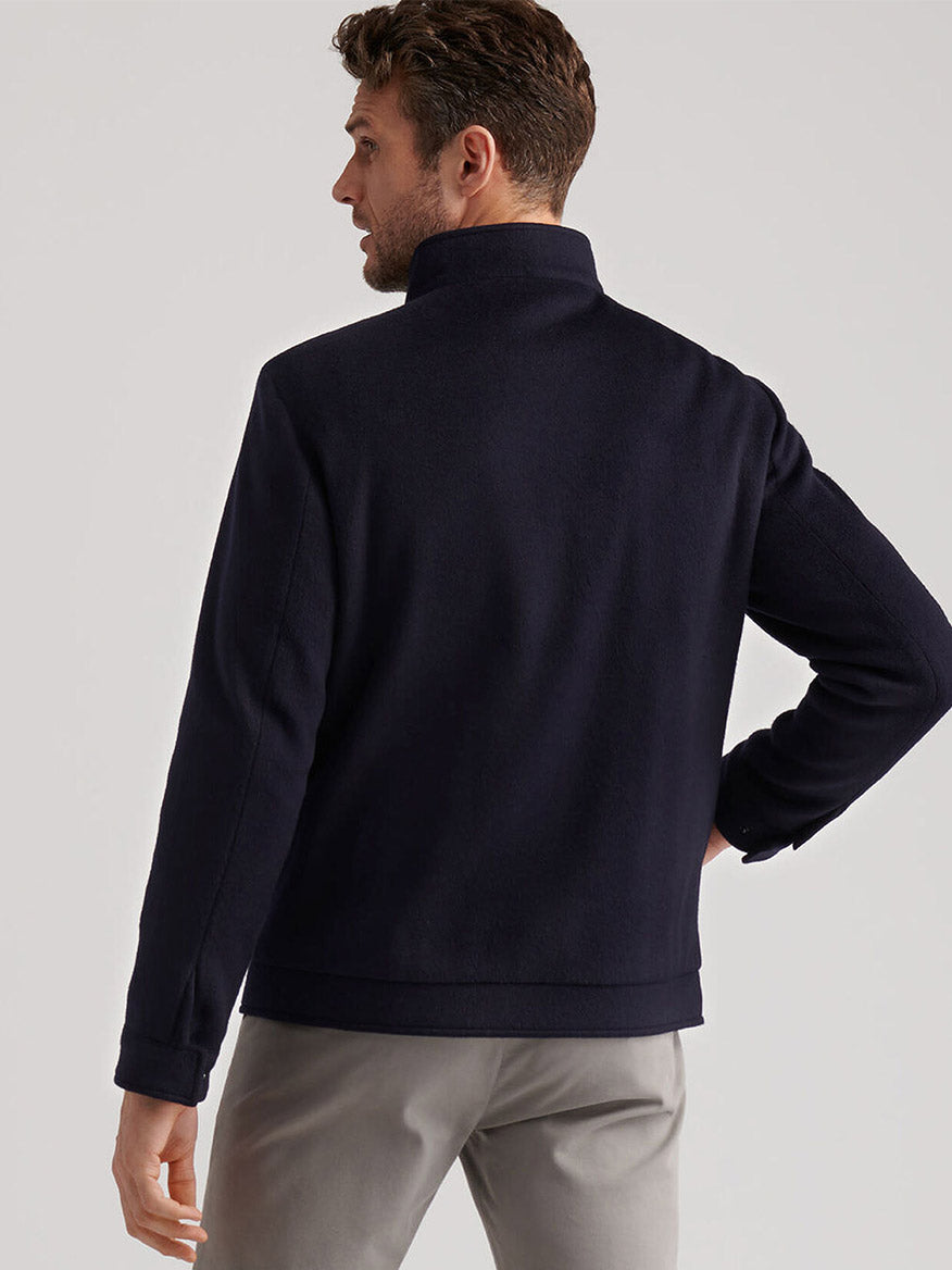 A man stands facing away, wearing the Peter Millar Crown Flex Merino Bomber in Navy and light gray pants against a plain background.