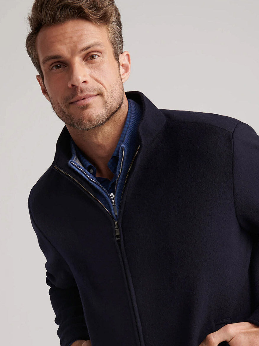 A man with short, wavy hair wears the Peter Millar Crown Flex Merino Bomber in Navy over a blue collared shirt, looking slightly past the camera against a plain background.