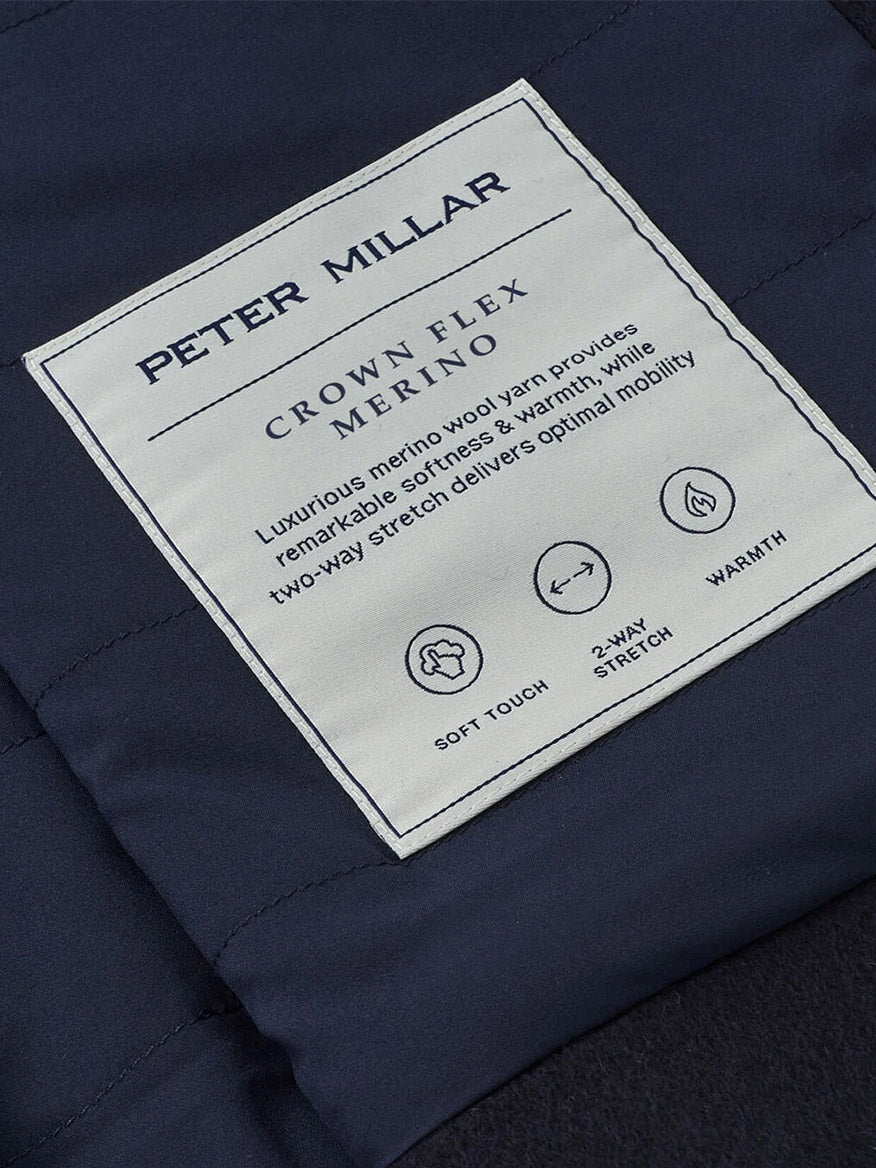 Close-up of the Peter Millar Crown Flex Merino Bomber label on navy fabric, highlighting its soft touch, two-way stretch, and superior warmth.