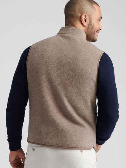 A man is shown from behind wearing the Peter Millar Crown Flex Merino Vest in Grain over a navy long-sleeve shirt and white pants—a versatile layer for any occasion.