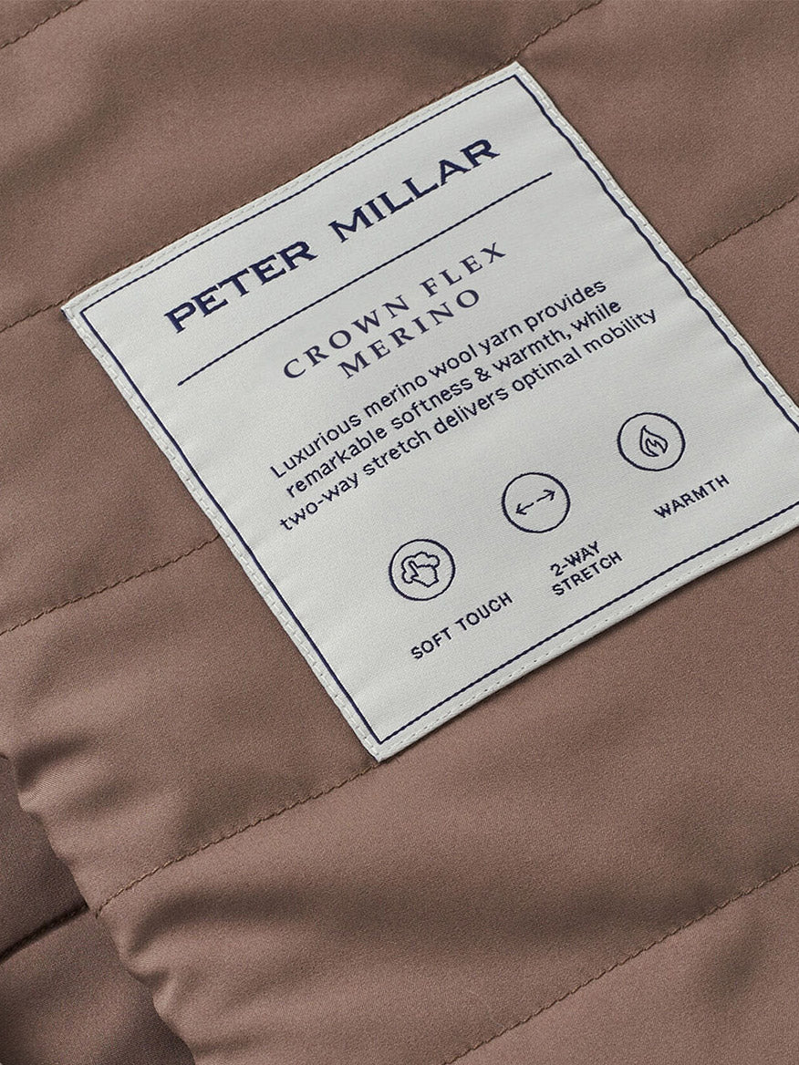 Close-up of the Peter Millar Crown Flex Merino Vest in Grain, crafted from stretch knit Merino wool with a white label, showcasing its soft touch, 2-way stretch, warmth, and versatility as a layering piece.