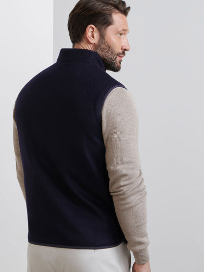 A man with brown hair and a beard wears the Peter Millar Crown Flex Merino Vest in Navy over a beige long-sleeve shirt and light pants, standing with his back turned.