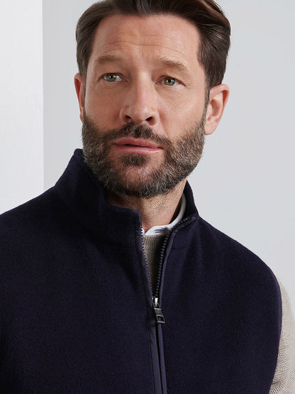 A man with short brown hair and a beard wears a navy Peter Millar Crown Flex Merino Vest over a light shirt, looking slightly to the side—a versatile layer designed for both style and comfort.
