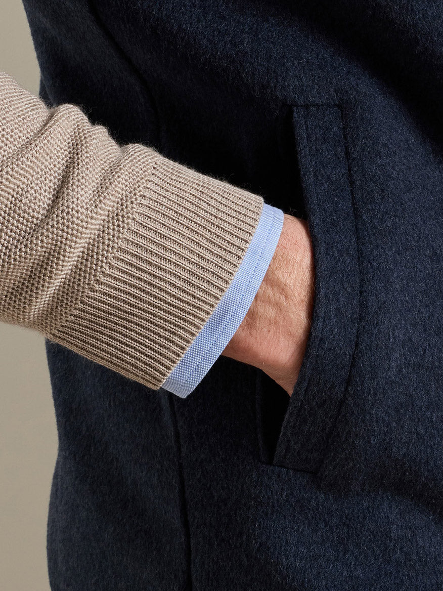 Close-up of a hand in the pocket of a Peter Millar Crown Flex Merino Vest in Atlantic Blue, worn over a beige sweater and light blue shirt.