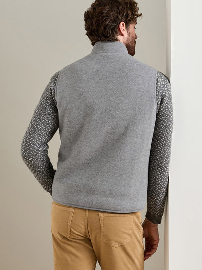 A man viewed from behind wears a Peter Millar Crown Flex Merino Vest in British Grey over a patterned stretch-knit Merino sweater and tan pants.