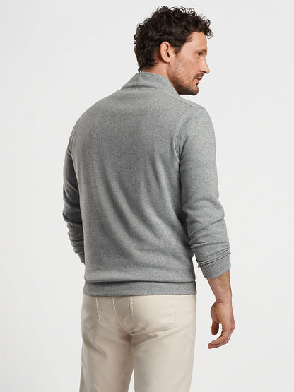 A man wearing the Peter Millar Crown Sweater Fleece Quarter-Zip in Gale Grey and beige pants, made from recycled materials, is standing and facing away from the camera.