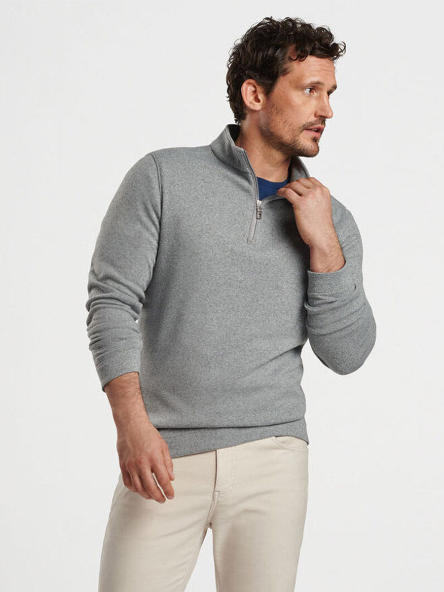 A man wearing the Peter Millar Crown Sweater Fleece Quarter-Zip in Gale Grey, made from recycled materials, and beige pants stands against a white background, looking to the side.