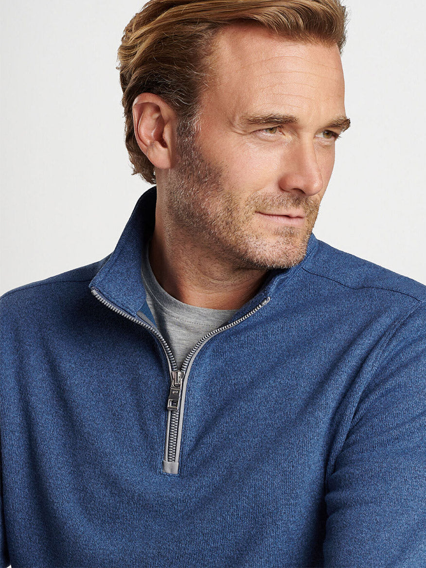 A man with light brown hair wearing the Peter Millar Crown Sweater Fleece Quarter-Zip in Ocean Blue over a gray shirt gazes to the side against a plain background.