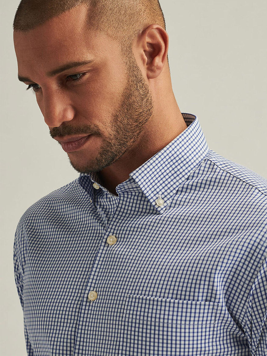 A man wearing a Peter Millar Derwent Performance Twill Sport Shirt in Sport Navy, featuring a blue and white checkered design with optimal breathability, looks downwards against a plain background.