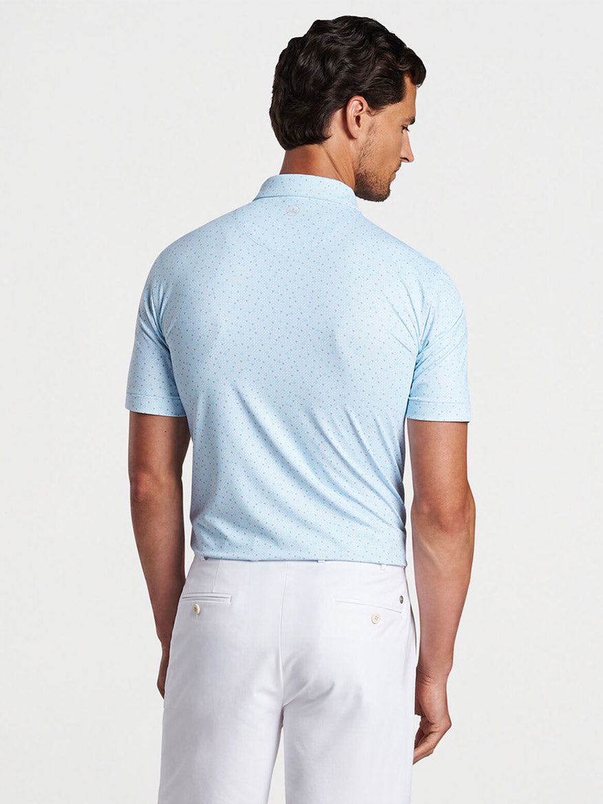 A man from behind wearing a Peter Millar Diamond In The Rough Performance Jersey Polo in Blue Frost and white pants.