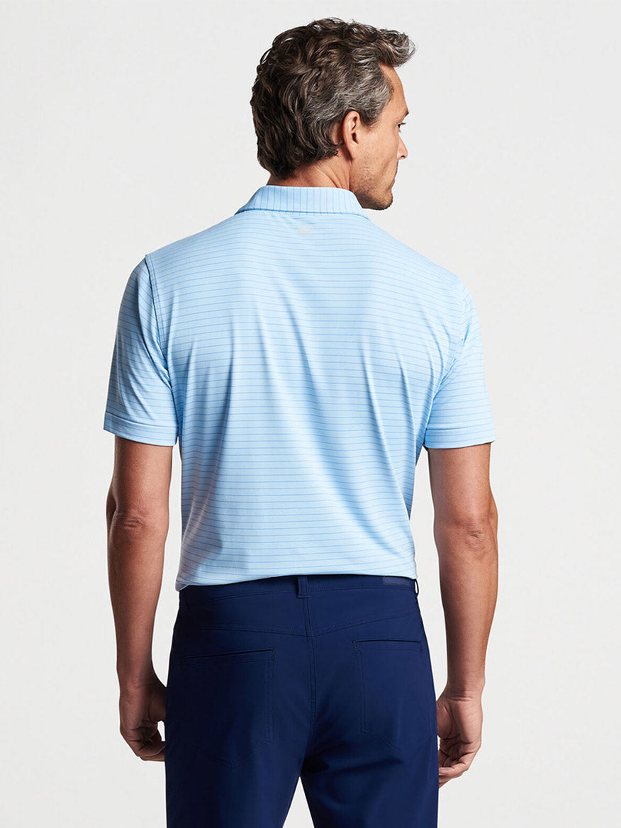 Man wearing a Peter Millar Duet Performance Jersey Polo in Blue Frost and navy trousers, viewed from behind.