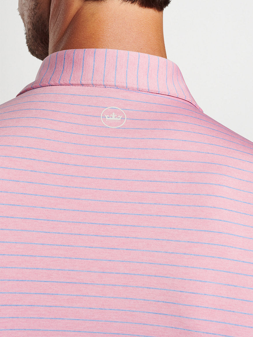 Close-up view of a person wearing a pink and white striped Peter Millar Duet Performance Jersey Polo in Spring Blossom with UPF 50+ sun protection and a logo on the collar.