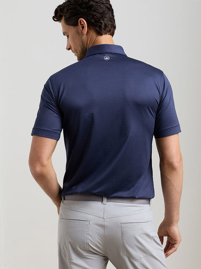 A man stands facing away in the Peter Millar Empire Performance Jersey Polo in navy (UPF 50+), paired with light gray pants, his right hand at his side.