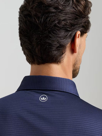 A man with dark hair is seen from behind wearing the Peter Millar Empire Performance Jersey Polo in navy, featuring a small white crown logo below the collar and crafted from comfortable four-way stretch fabric.