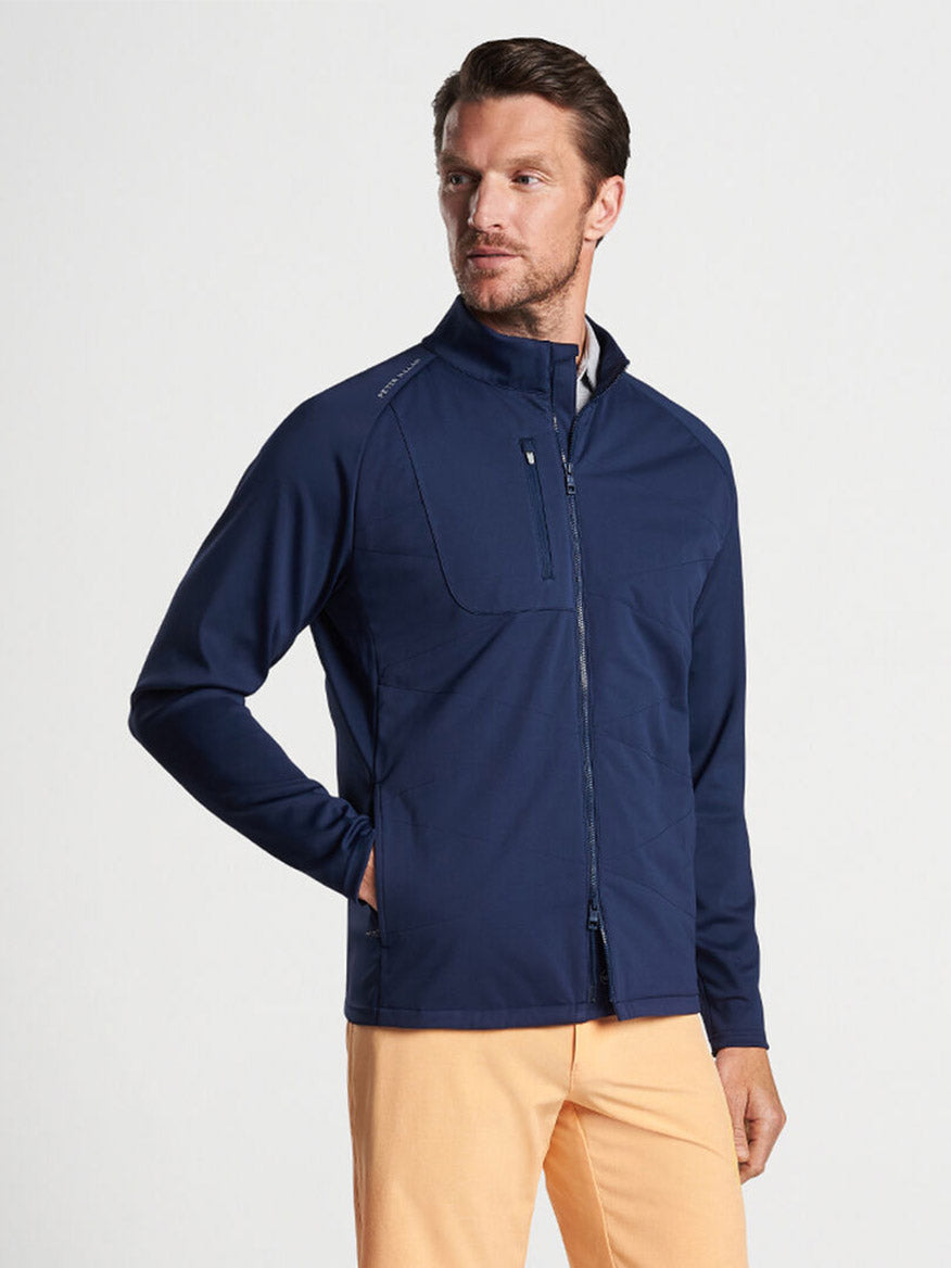 Man modeling a Peter Millar Merge Hybrid Jacket in Navy, crafted from performance fabric for lightweight warmth, paired with yellow pants.