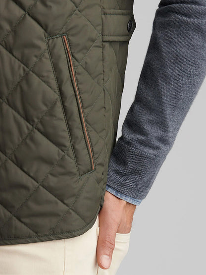 A person wearing the Peter Millar Essex Vest in Dark Olive, a blue-gray sweater, and beige pants with their hand resting by their side.